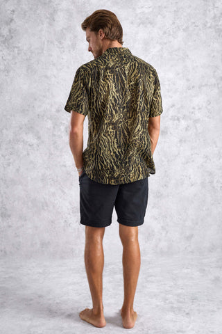 Man wearing a patterned shirt and black shorts against a textured gray background